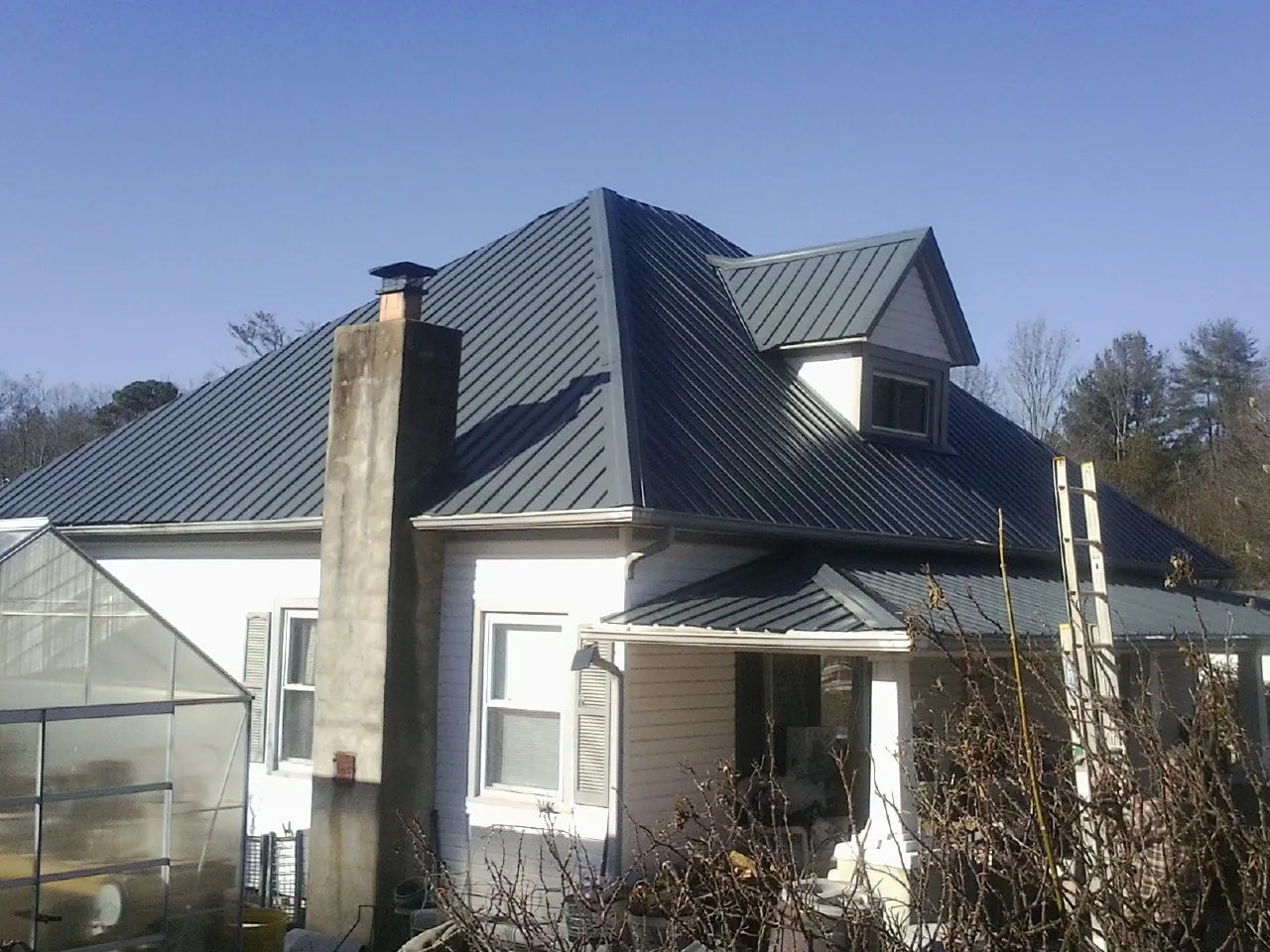 Dark blue standing seam metal roof on a white farmhouse with dormer — Slate & Tile Roof Repair by Roofing Brothers in Finley