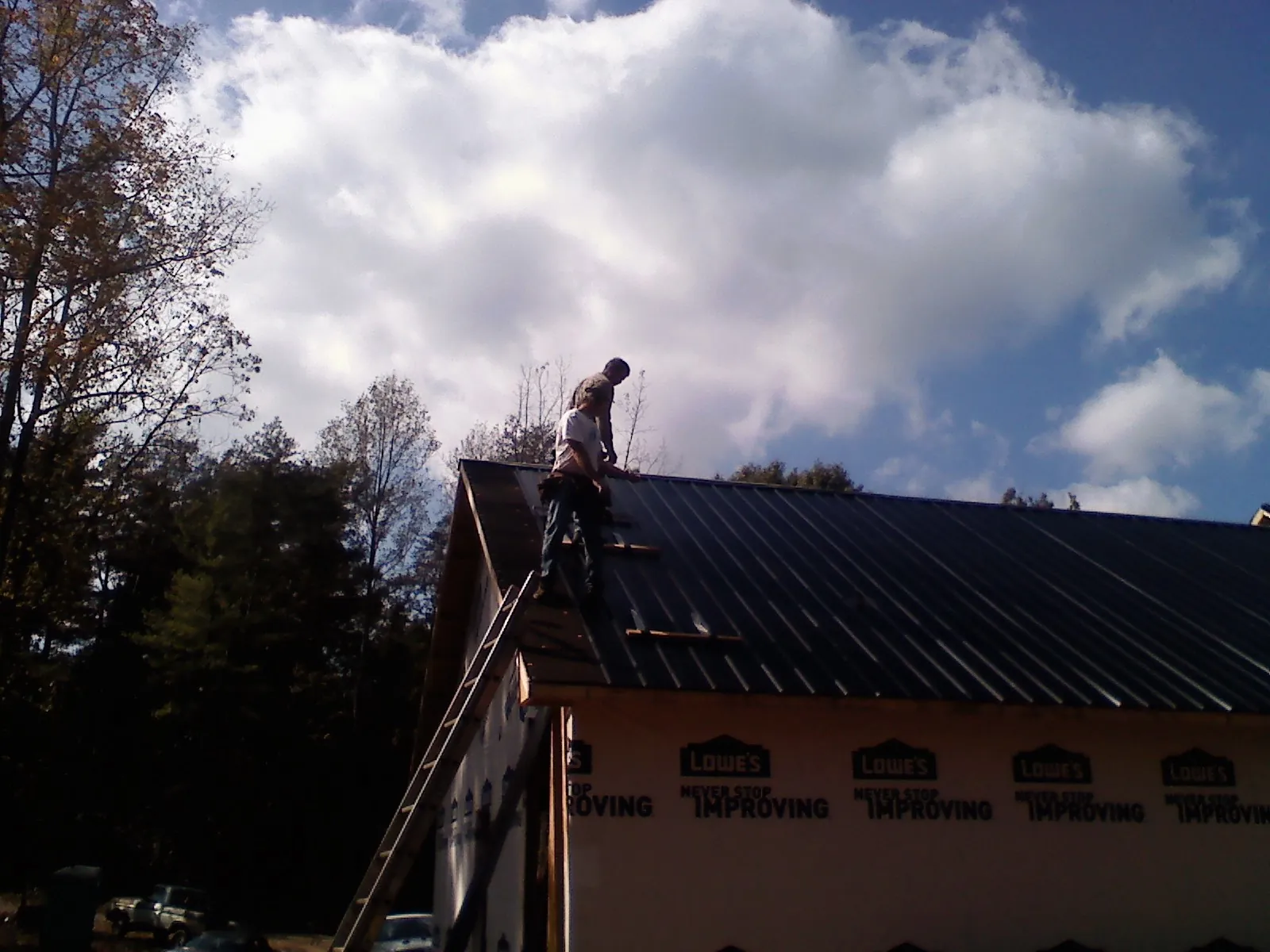 Roofer fastening dark metal panels high against a cloudy sky, from a Roof Inspection job in Finley