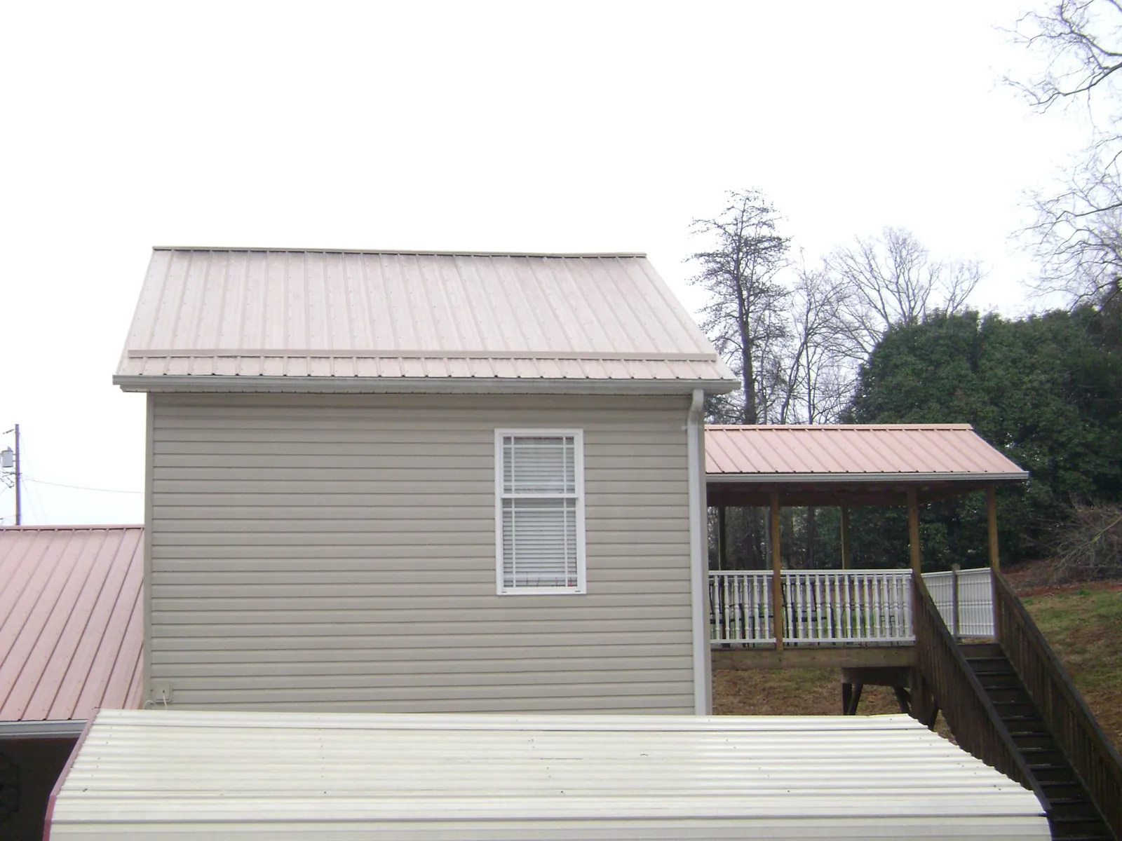 Tan metal roofs on a two story addition and attached porch, from a Roof Replacement job in Finley